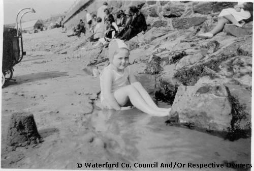 Tramore, County Waterford. Marie Stokes sitting in the rock pools near the sea wall in Tramore. Holiday makers shown sitting on the strand  beneath the wall
