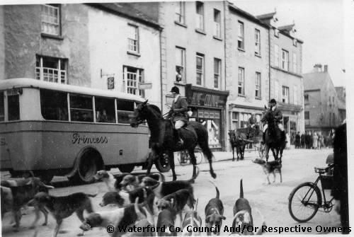 Clonmel, County Tipperary. The hunt on its way through Clonmel. Hounds, bicycles, a bus, riders, a horse and cart and pedestrians sharing a shopping street
